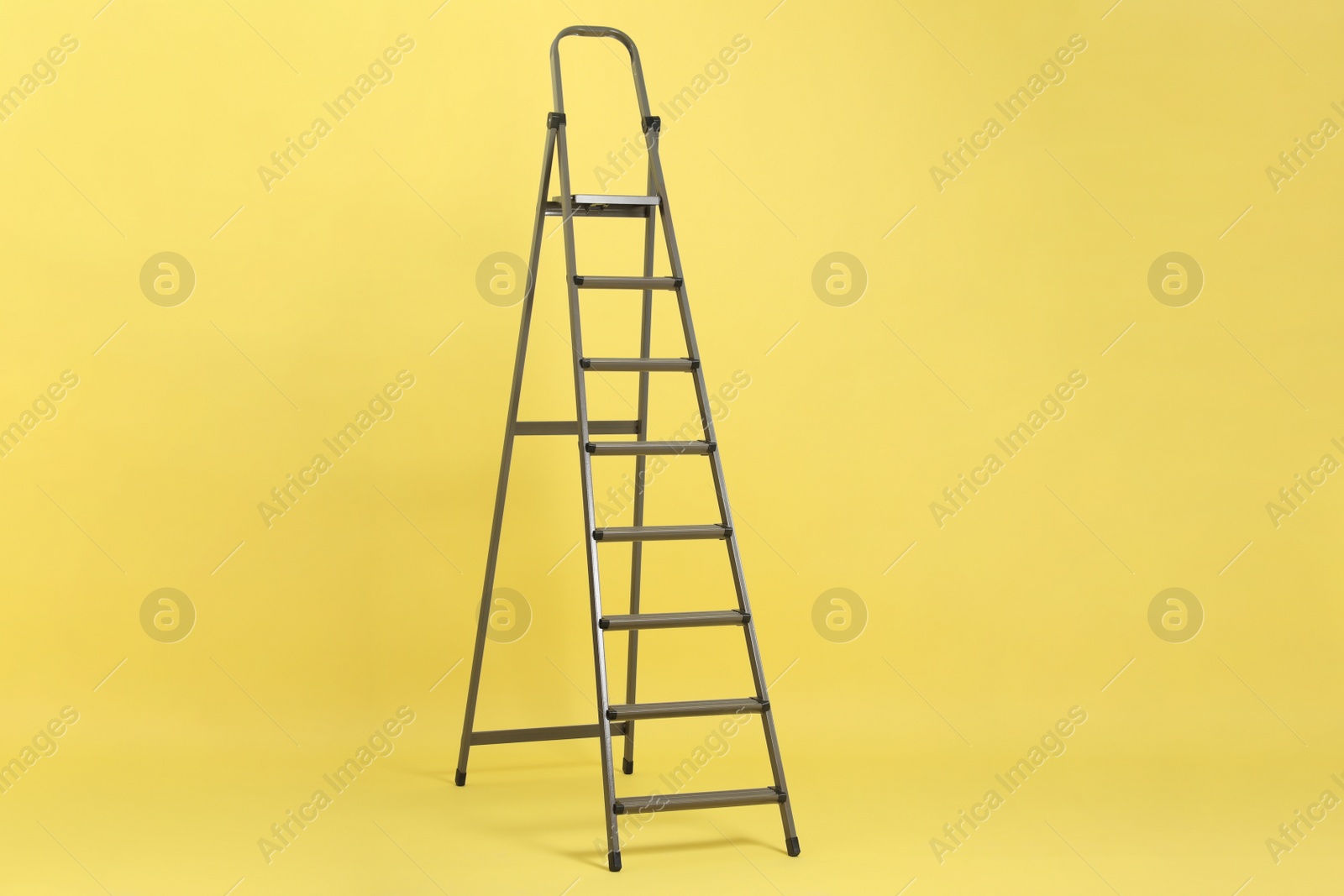 Photo of Modern metal stepladder on yellow background. Construction tool