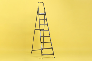 Modern metal stepladder on yellow background. Construction tool