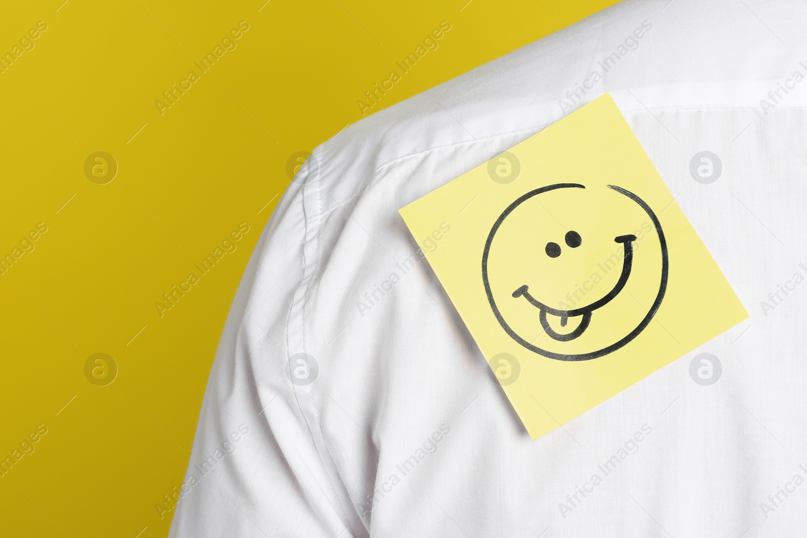 Photo of Man with funny face sticker on back against yellow background, closeup. April fool's day