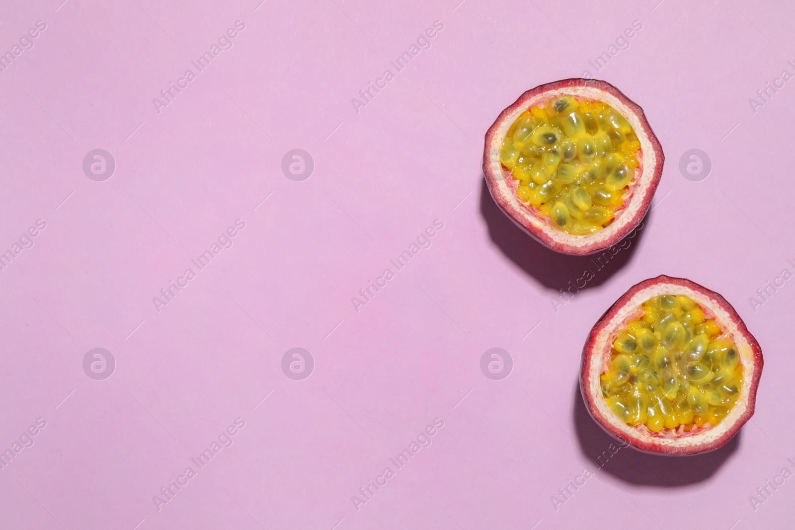 Photo of Halves of passion fruit (maracuya) on pink background, flat lay. Space for text