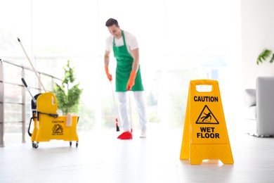 Safety sign with phrase "CAUTION WET FLOOR" and young man on background