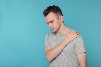 Young man suffering from pain in his shoulder on light blue background, space for text. Arthritis symptoms