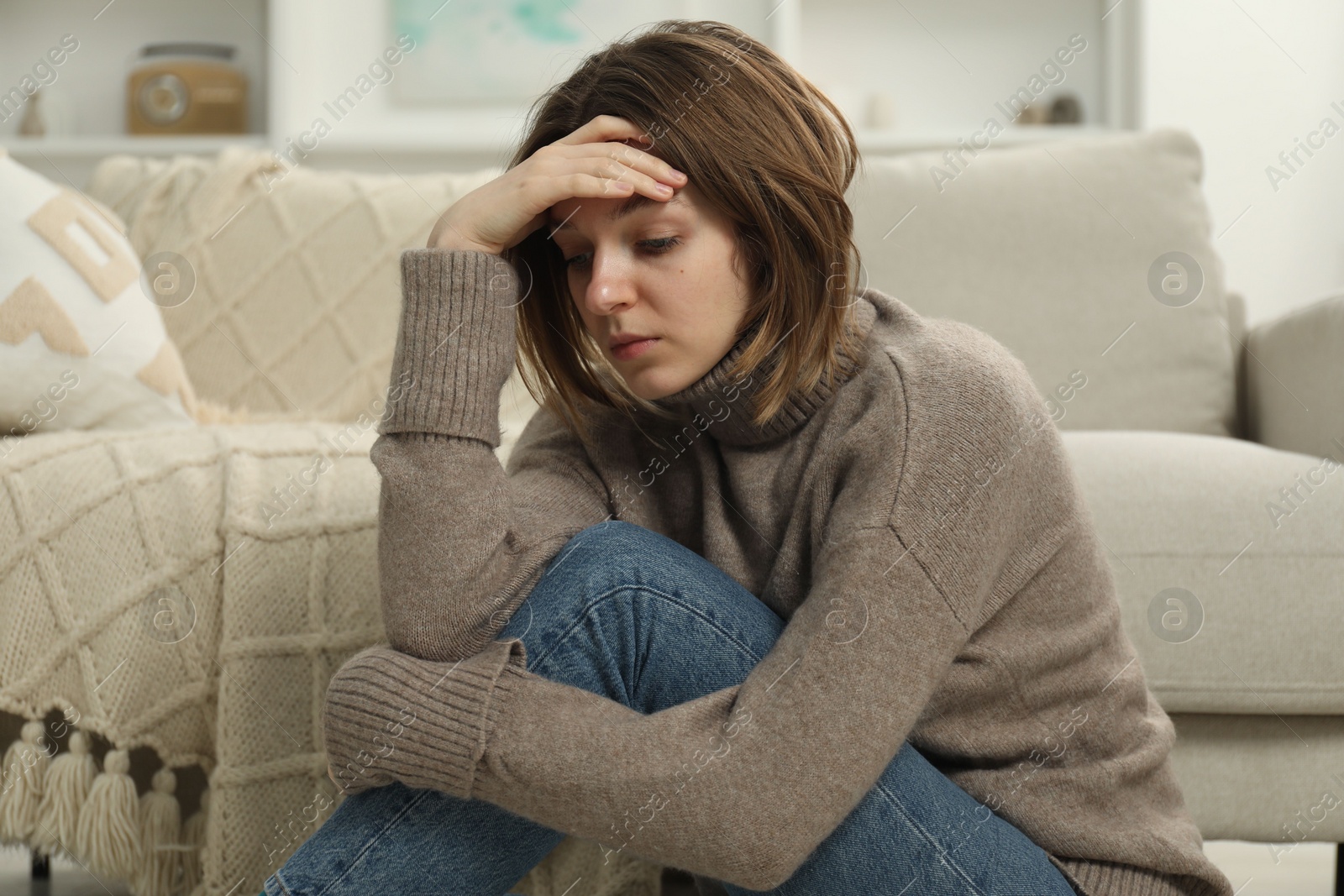 Photo of Sad young woman sitting near sofa at home