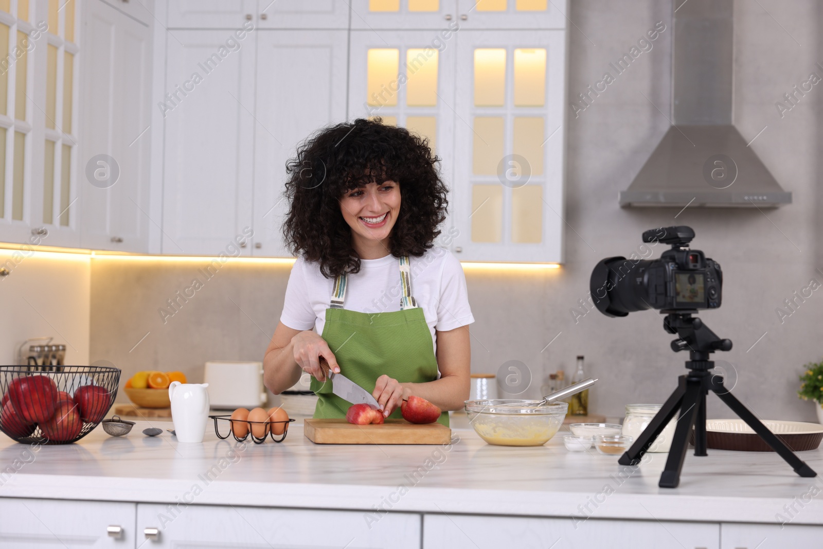 Photo of Smiling food blogger cooking while recording video in kitchen