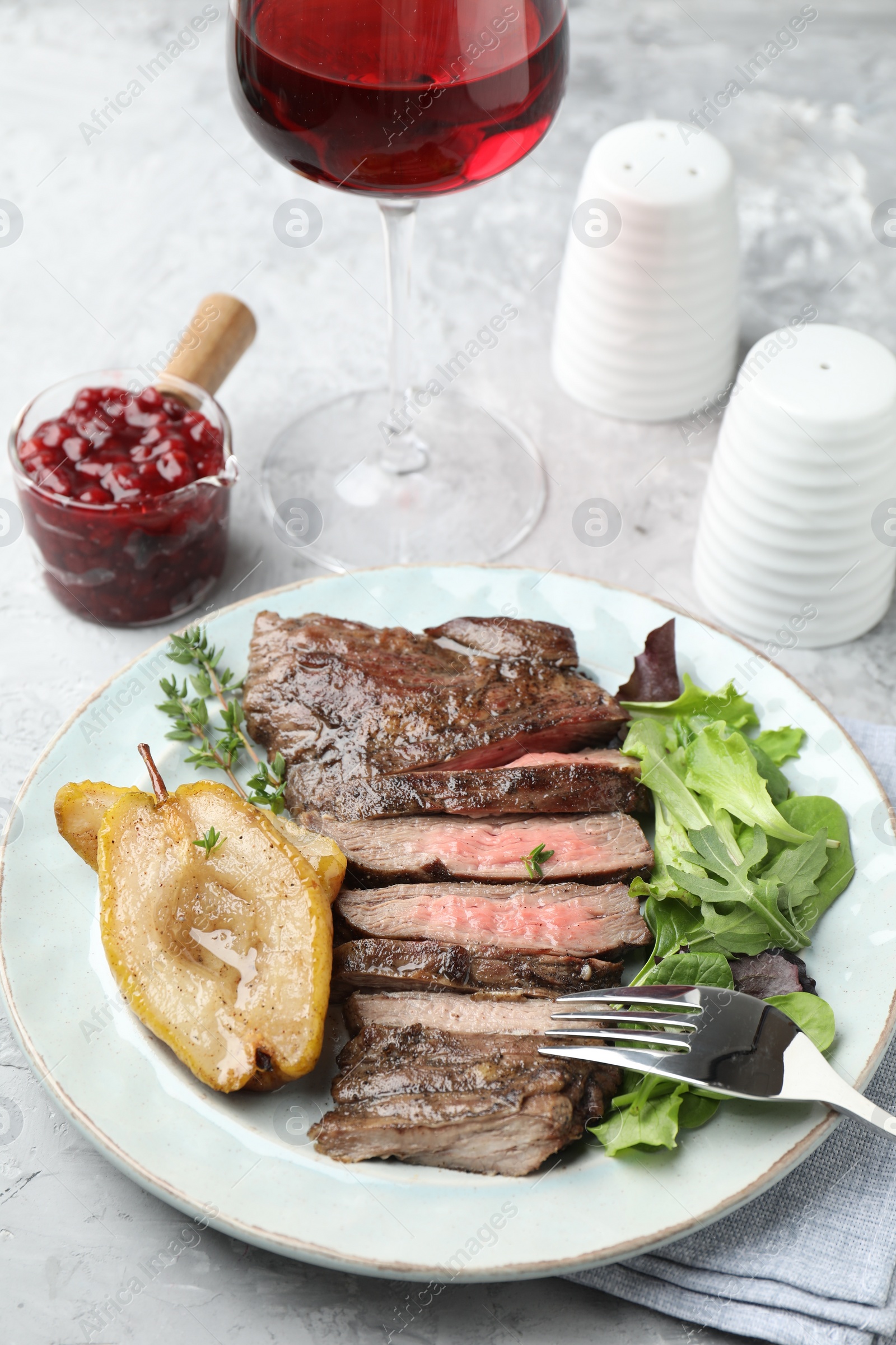 Photo of Delicious roasted beef meat, caramelized pear and greens served on light table