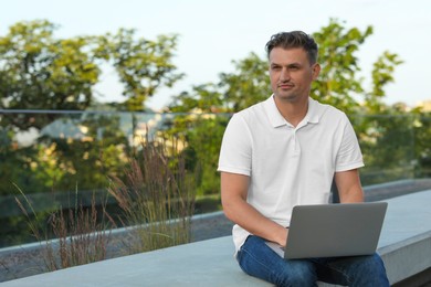 Handsome man using laptop on stone bench outdoors. Space for text