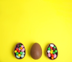 Photo of Tasty chocolate eggs with colorful candies on yellow background, flat lay. Space for text