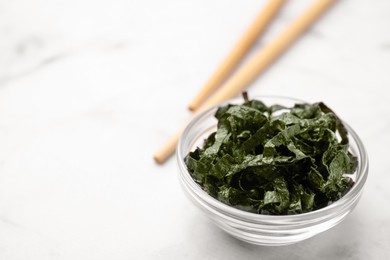 Photo of Chopped nori sheets with chopsticks on white marble table, closeup. Space for text