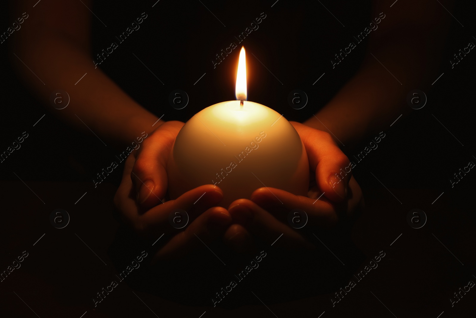 Photo of Woman holding burning candle in hands on black background, closeup