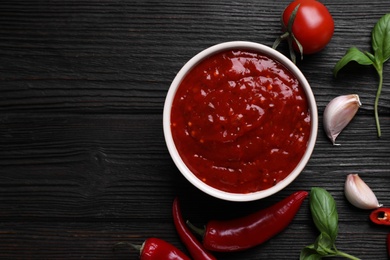 Flat lay composition with bowl of chili sauce and ingredients on wooden table. Space for text