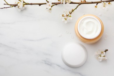 Photo of Jar of face cream, tree branch and flowers on white marble table, flat lay. Space for text