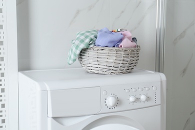 Photo of Wicker laundry basket with different clothes on washing machine in bathroom
