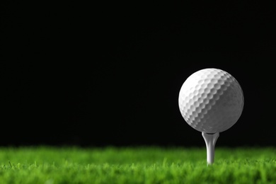 Photo of Golf ball with tee on artificial grass against black background, space for text