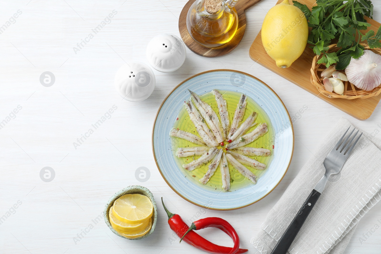 Photo of Tasty pickled anchovies with spices and products on white wooden table, flat lay. Space for text