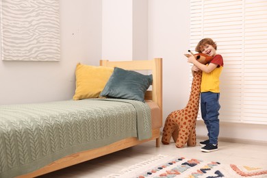 Photo of Cute little boy with plush giraffe in room. Child's toy