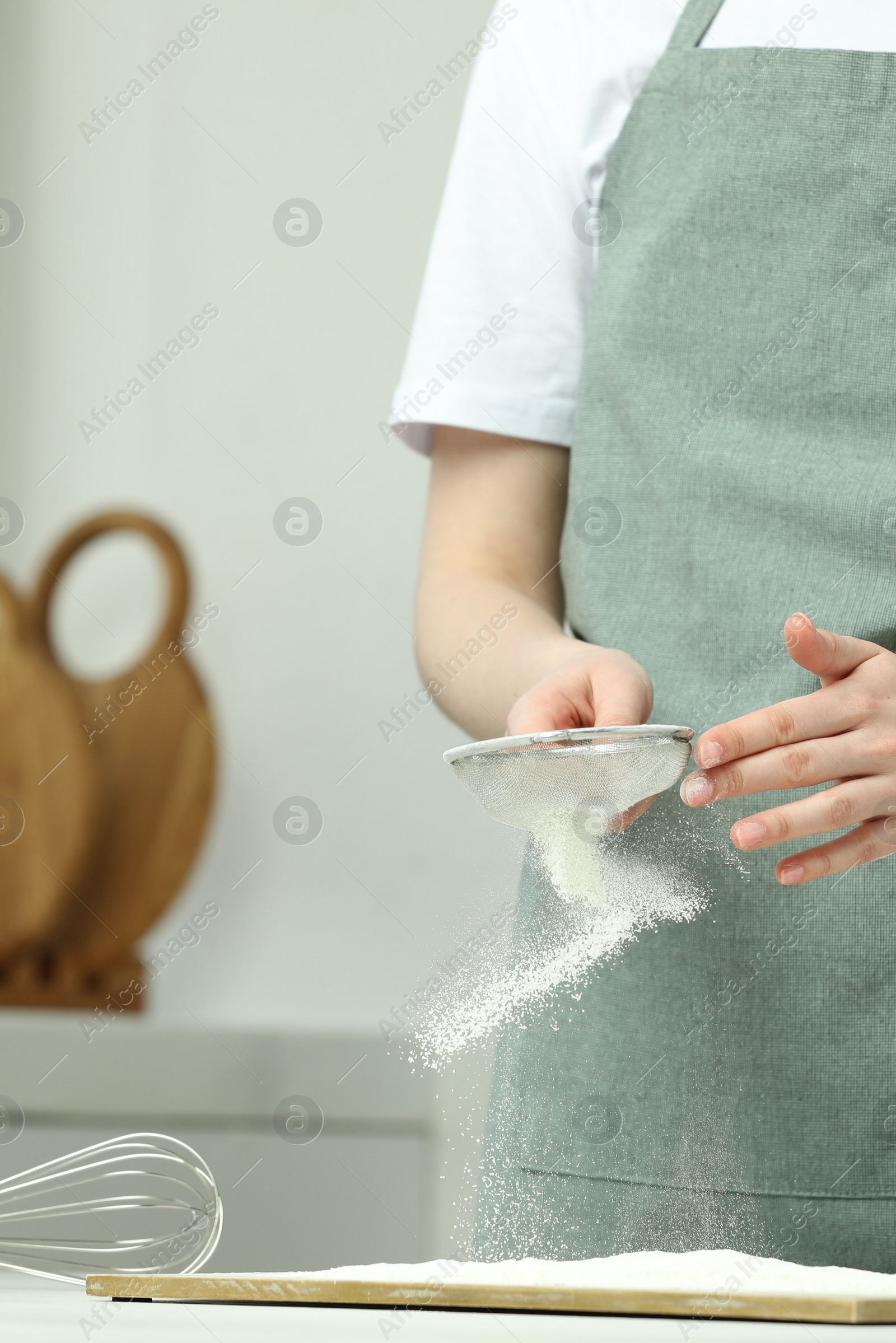 Photo of Woman sieving flour at table in kitchen, closeup. Space for text