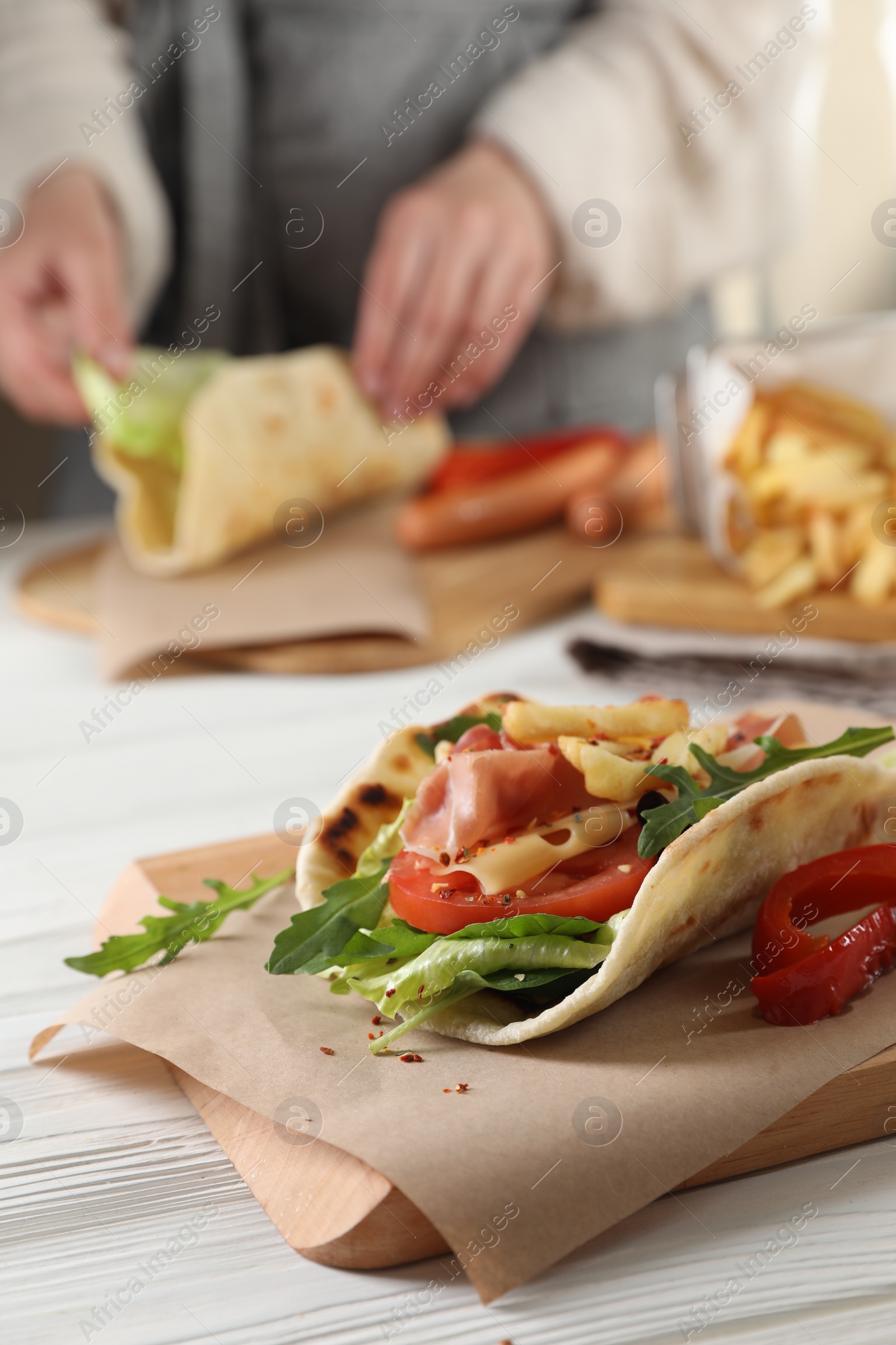 Photo of Woman cooking delicious pita wrap with jamon, cheese and vegetables at wooden table. Focus on dish