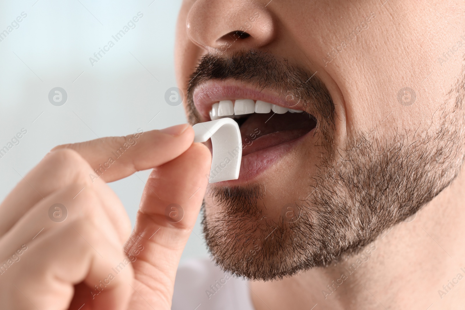 Photo of Man putting chewing gum into mouth on light background, closeup