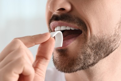 Photo of Man putting chewing gum into mouth on light background, closeup