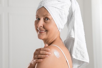 Photo of Happy woman applying body cream onto shoulder near white wall