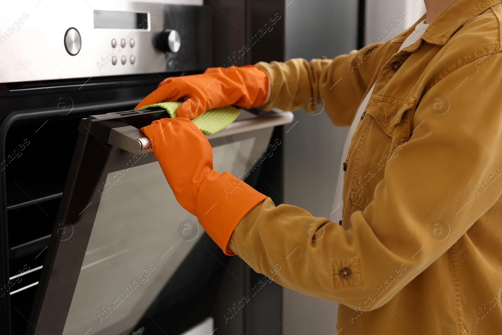 Photo of Woman with microfiber cloth cleaning electric oven in kitchen, closeup