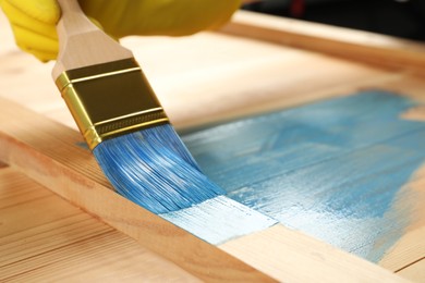 Worker applying blue paint onto wooden surface, closeup. Space for text