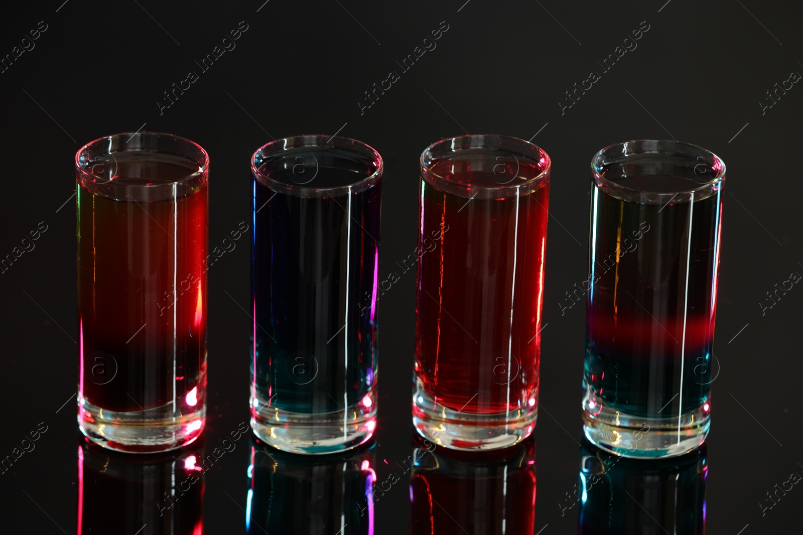Photo of Different shooters in shot glasses on mirror surface against blurred background, closeup Alcohol drink