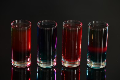 Different shooters in shot glasses on mirror surface against blurred background, closeup Alcohol drink