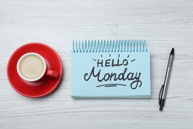 Message Hello Monday written in notebook, pen and cup of coffee on white wooden desk, flat lay