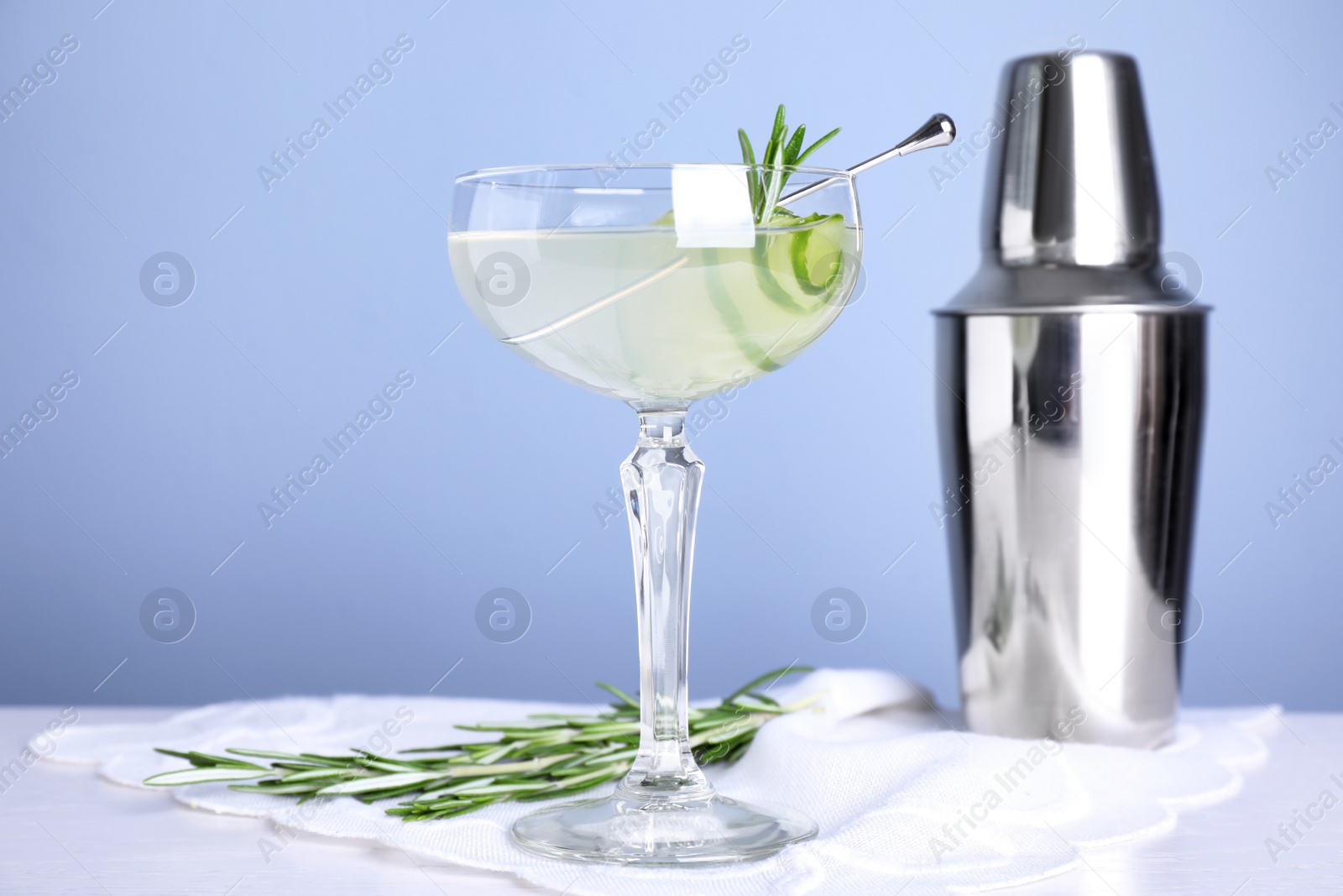 Photo of Glass of cucumber martini, shaker and rosemary on table against color background, space for text