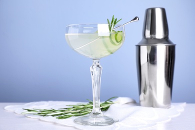Photo of Glass of cucumber martini, shaker and rosemary on table against color background, space for text