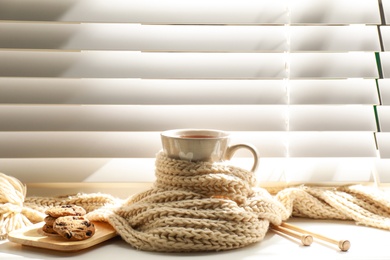 Cup of hot winter drink with scarf and cookies on windowsill indoors. Space for text