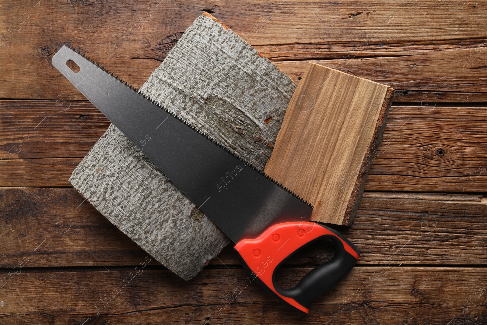 Photo of Saw with colorful handle and logs on wooden background, top view