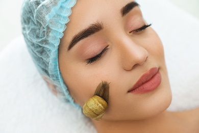 Photo of Young woman receiving snail facial massage in spa salon, closeup