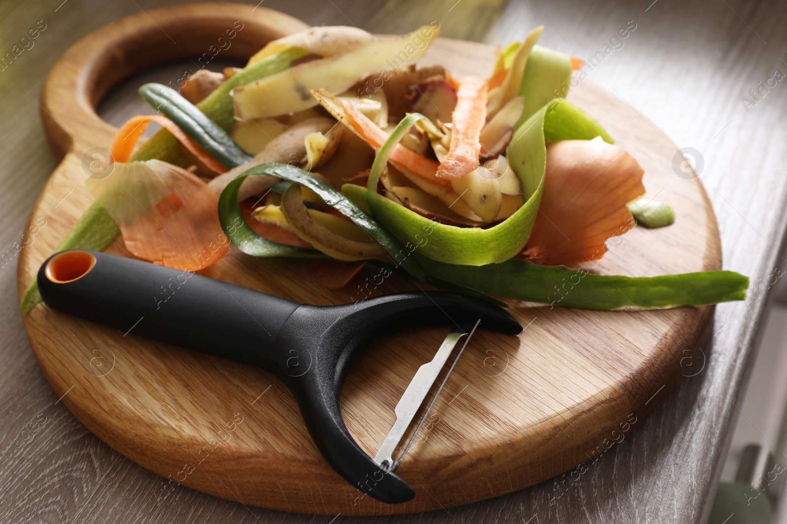 Photo of Peels of fresh vegetables and peeler on wooden table, closeup