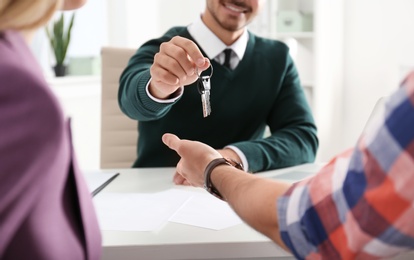 Photo of Real estate agent giving keys to young couple in office