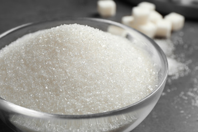 Photo of Granulated sugar in bowl on grey table, closeup