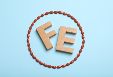 Photo of Wooden letters FE and pills on light blue background, flat lay. Anemia concept