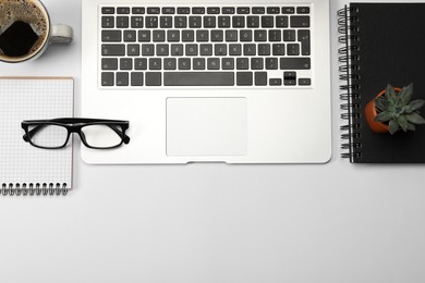 Modern laptop, notebooks, houseplant, glasses and cup of coffee on white background, flat lay. Space for text