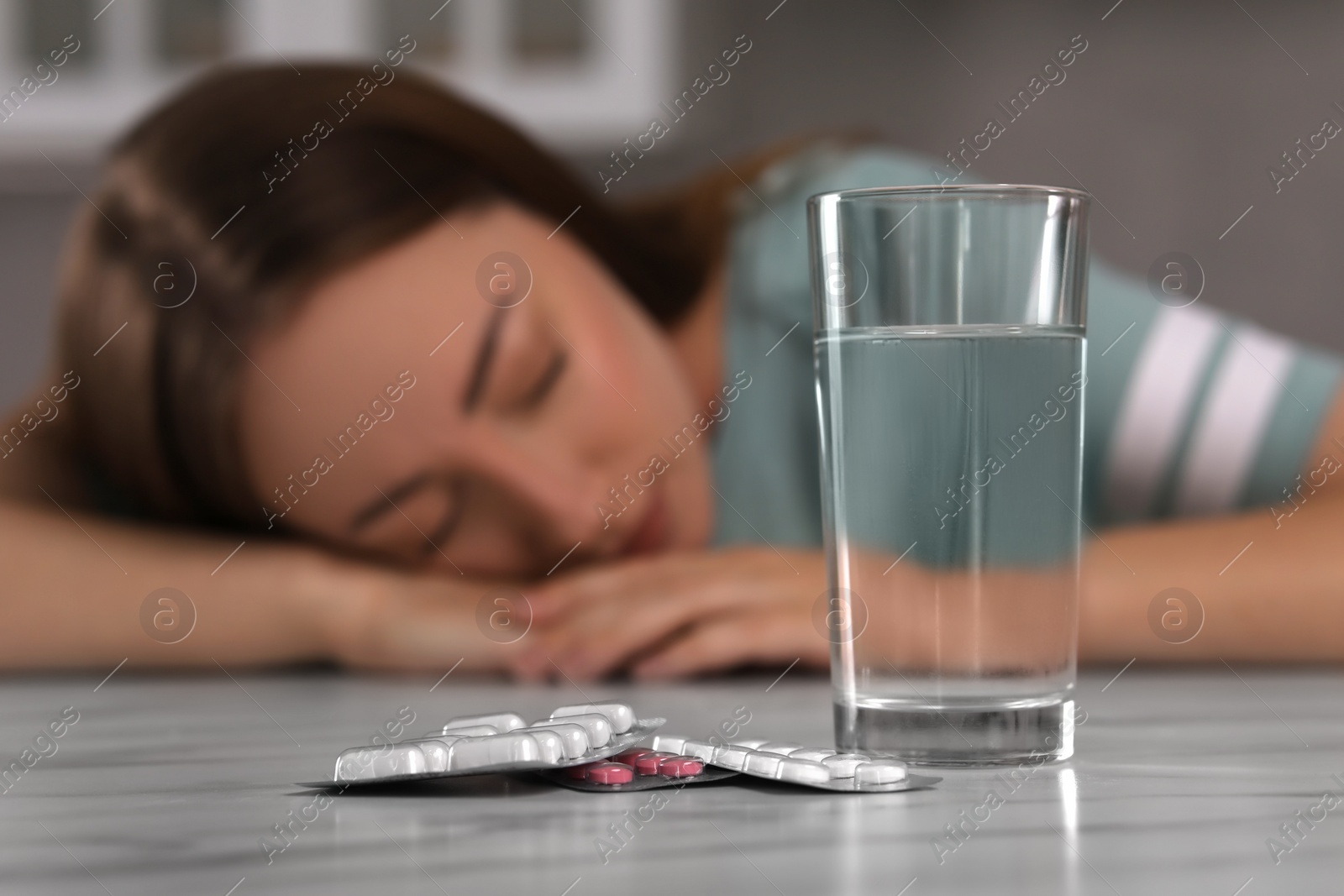 Photo of Woman sleeping at table with antidepressant pills and glass of water indoors, selective focus