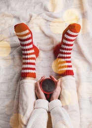 Image of Woman relaxing with cup of hot winter drink on knitted plaid, top view. Cozy season