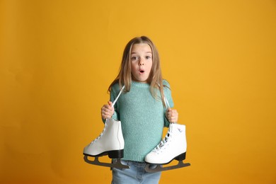 Photo of Surprised little girl in turquoise knitted sweater with skates on yellow background