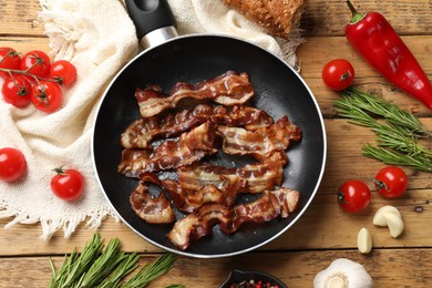 Delicious bacon slices in frying pan and products on wooden table, flat lay