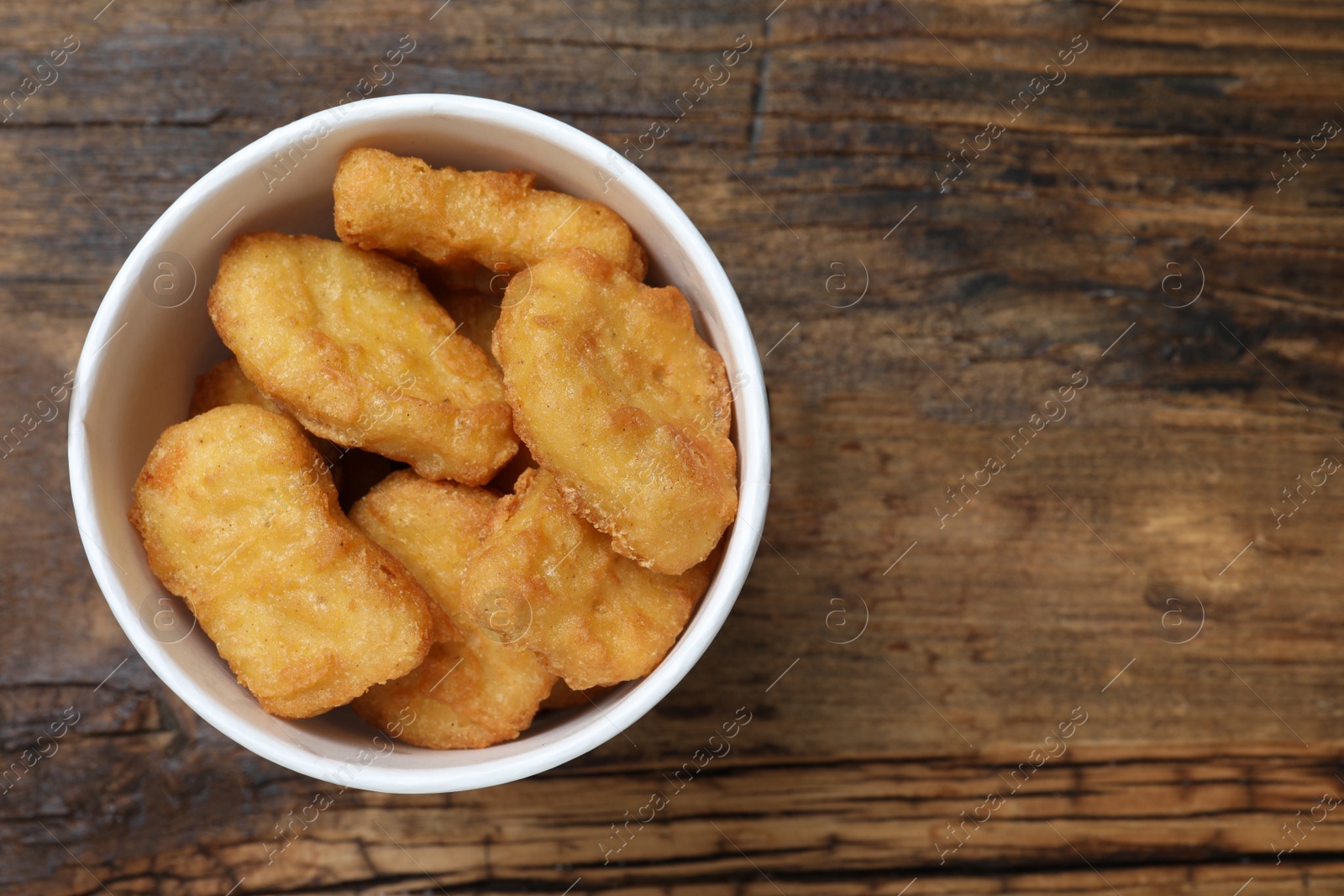 Photo of Bucket with tasty chicken nuggets on wooden table, top view. Space for text