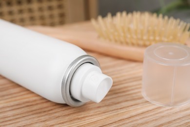 Photo of Dry shampoo spray near hairbrush on wooden table indoors, closeup