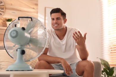 Photo of Man enjoying air flow from fan on sofa in living room. Summer heat