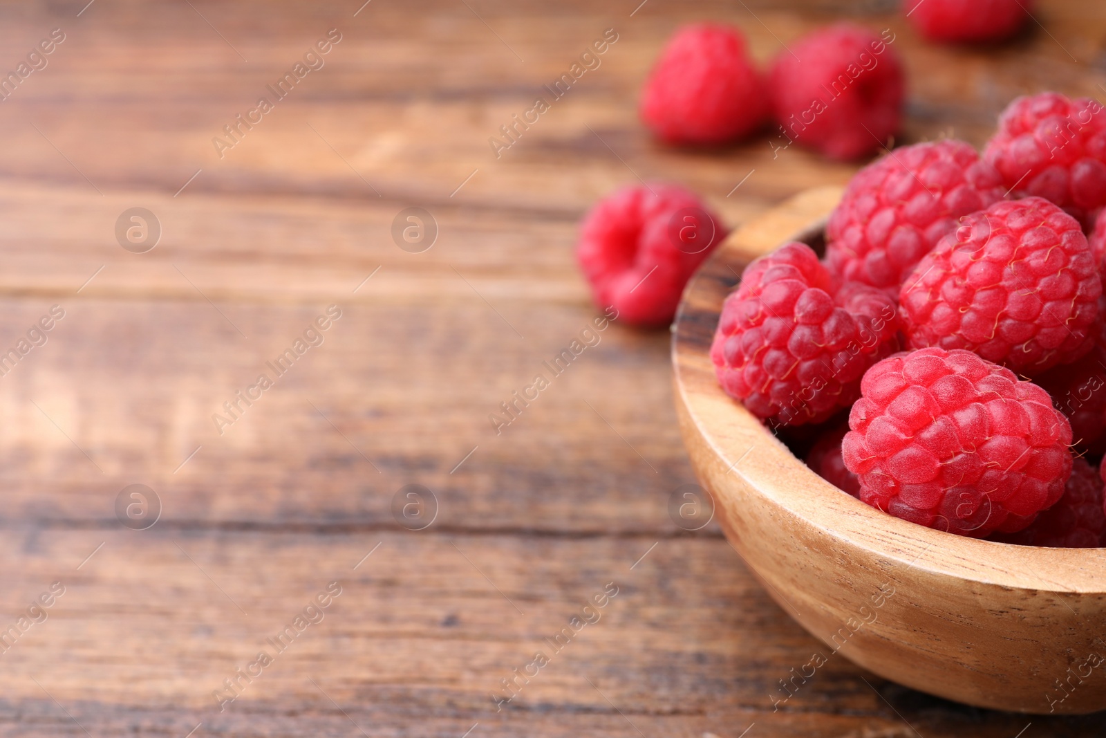 Photo of Tasty ripe raspberries in bowl on wooden table, closeup. Space for text