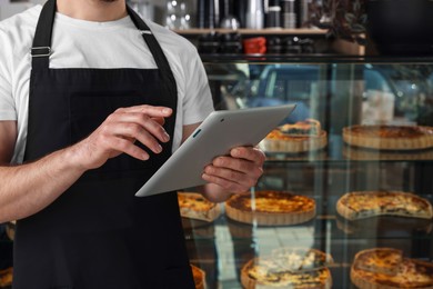 Photo of Seller with tablet near showcase in bakery shop, closeup. Space for text