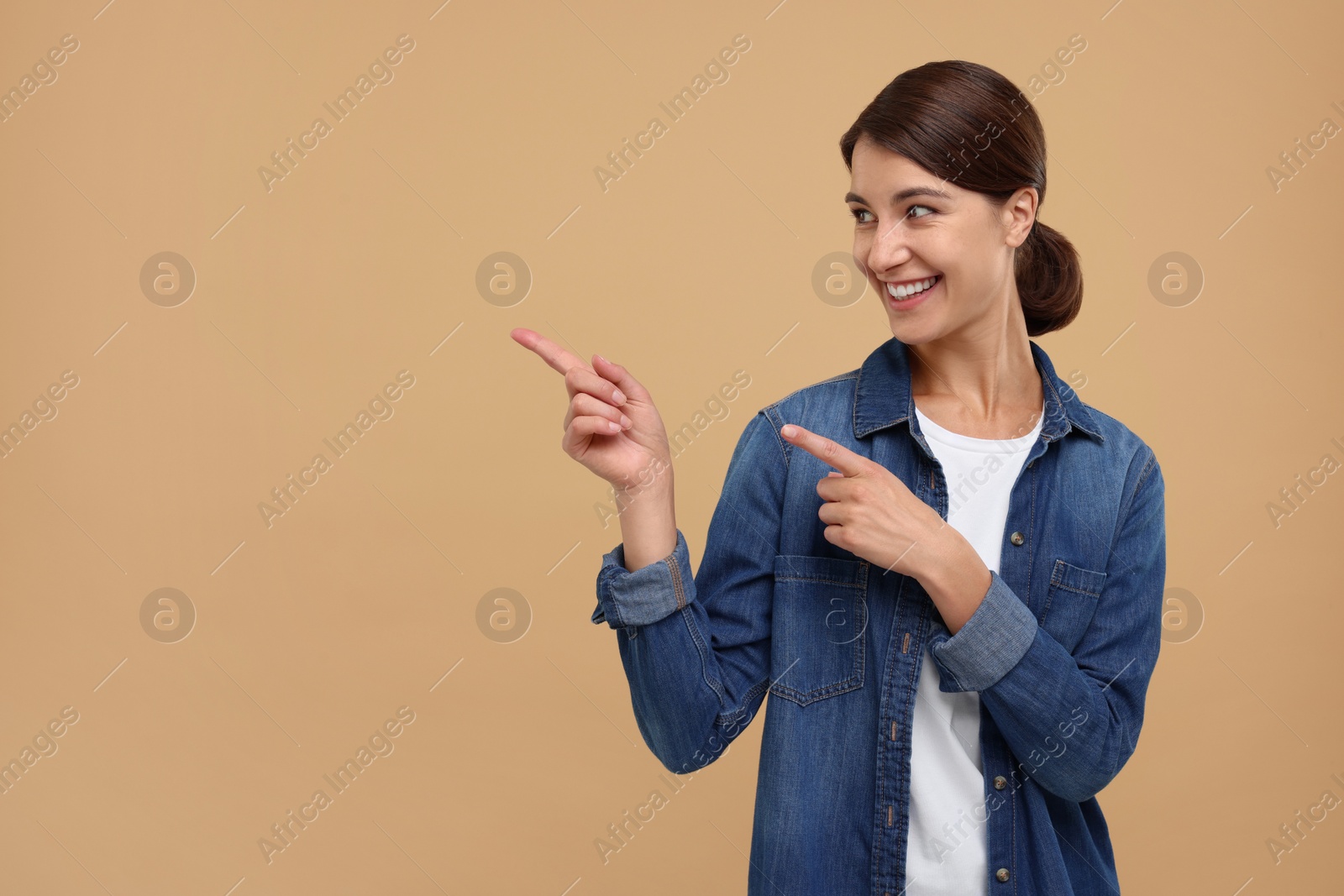 Photo of Special promotion. Happy woman pointing at something on beige background, space for text