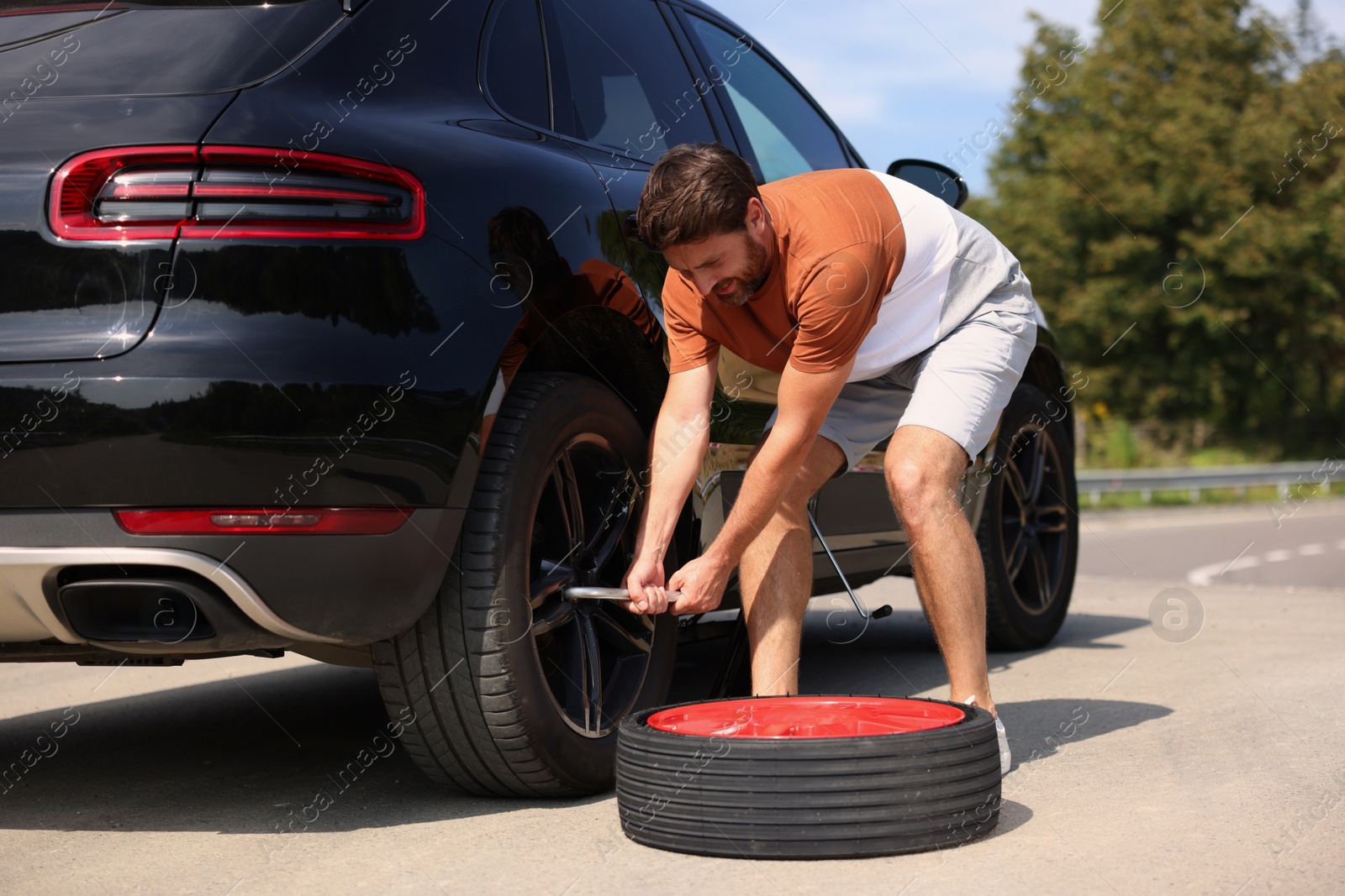 Photo of Man changing wheel of car on roadside outdoors